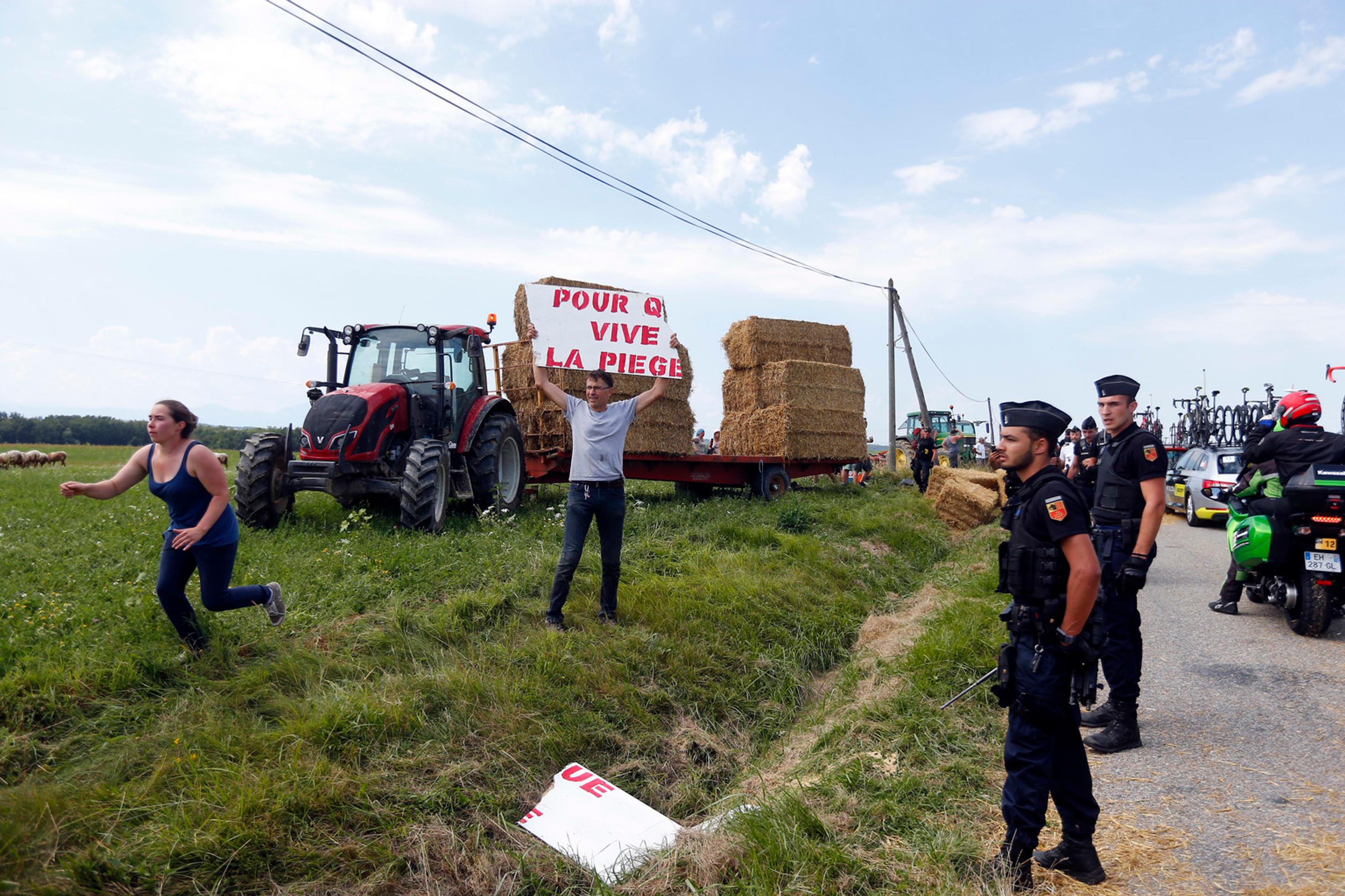 Policajti sledujú protestujúcich farmárov počas 16. etapy Tour de France.