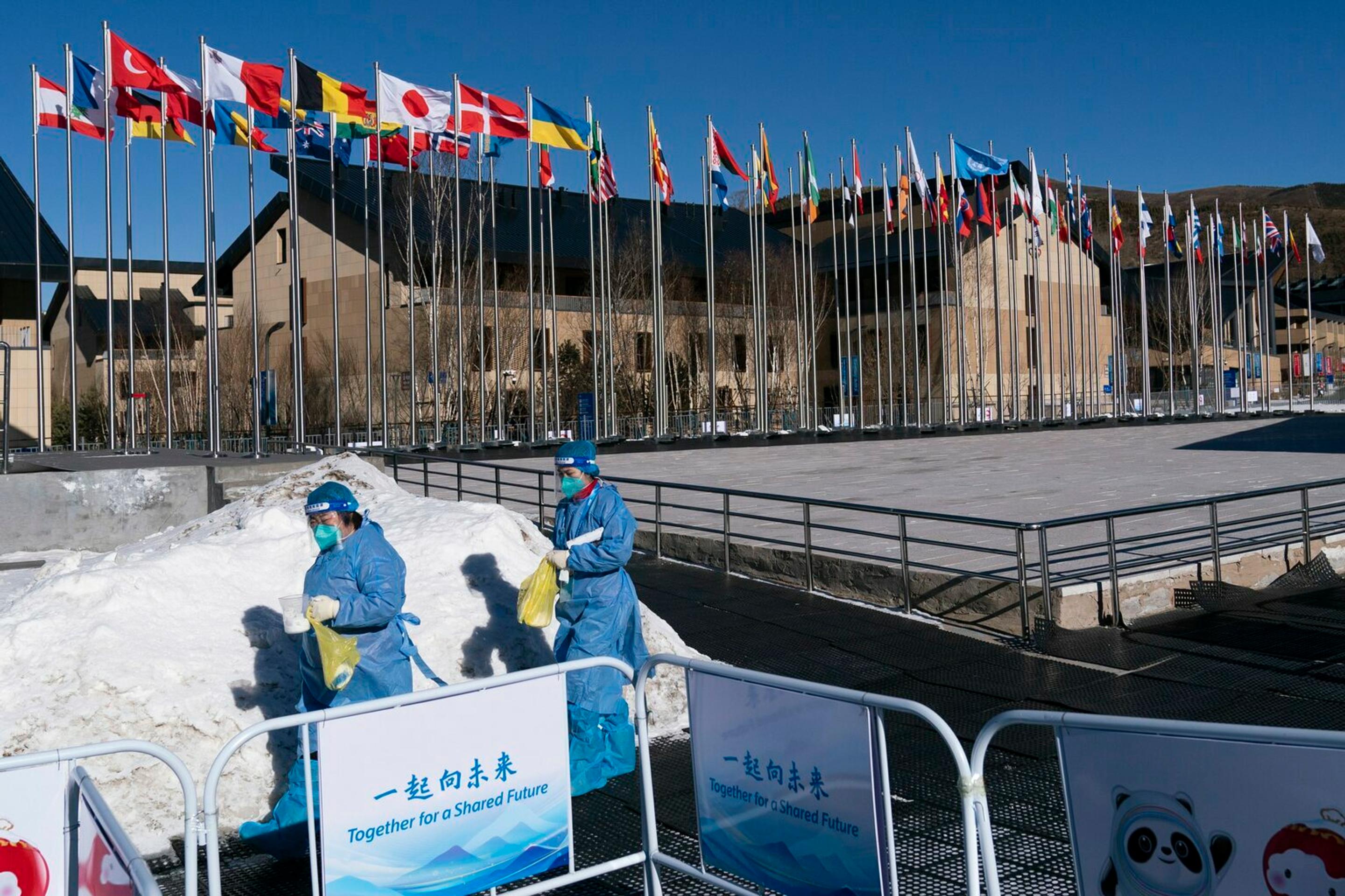 Zdravotníci v ochranných oblekoch smerujú do kancelárie v olympijskej dedine.