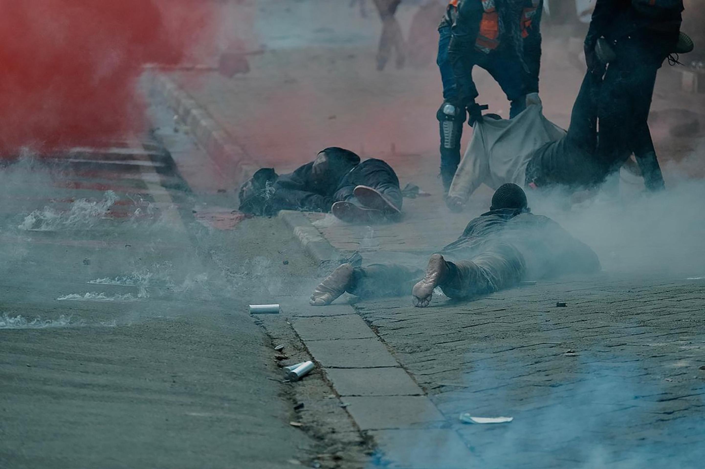 Zranení demonštranti ležia na hodníku po zásahu polície.