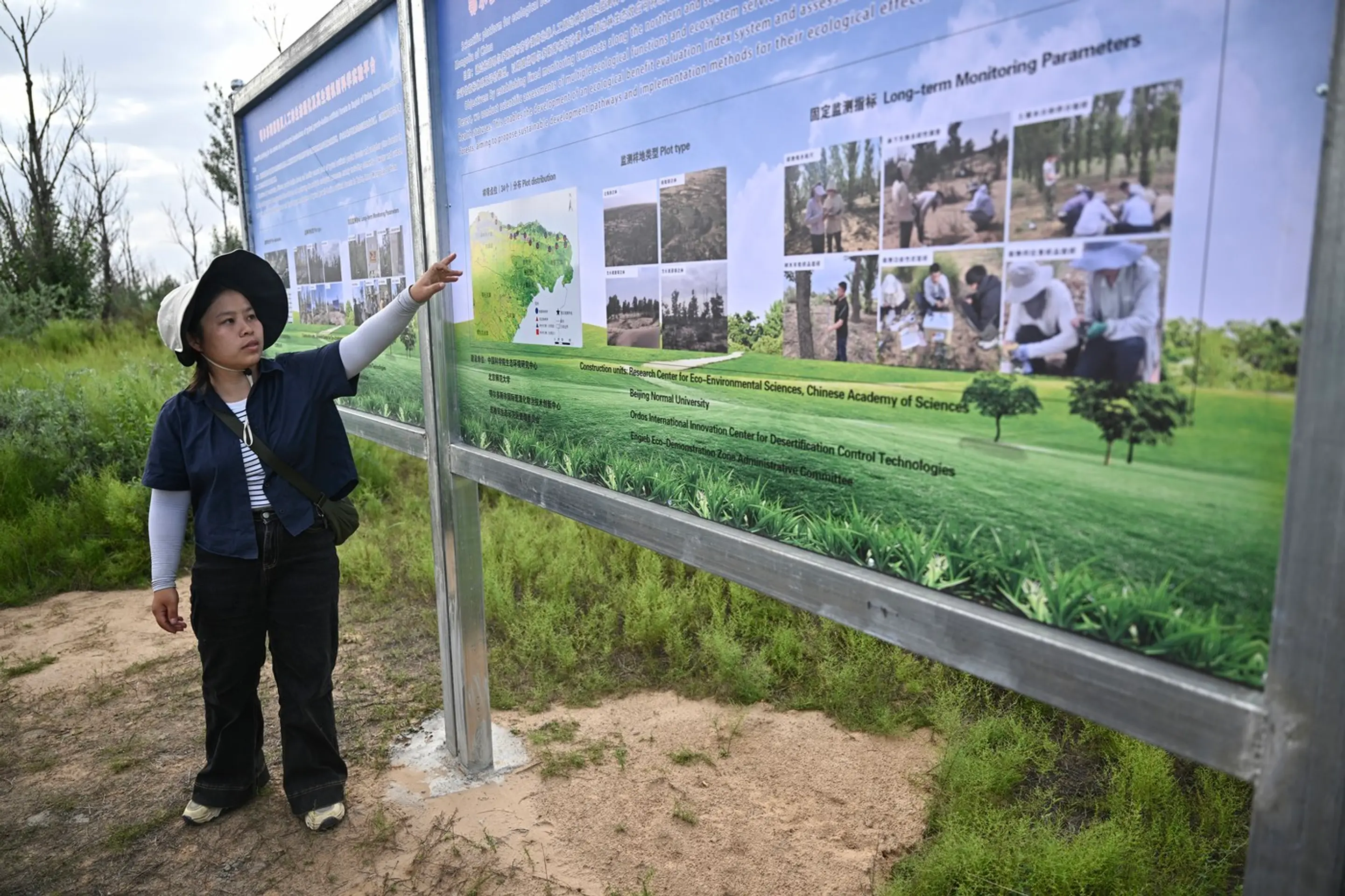Na tejto fotografii z 11. augusta 2025 študentka Zhang Yanping vysvetľuje projekt zalesňovania suchých a púštnych oblastí, známy ako „Veľký zelený múr“.