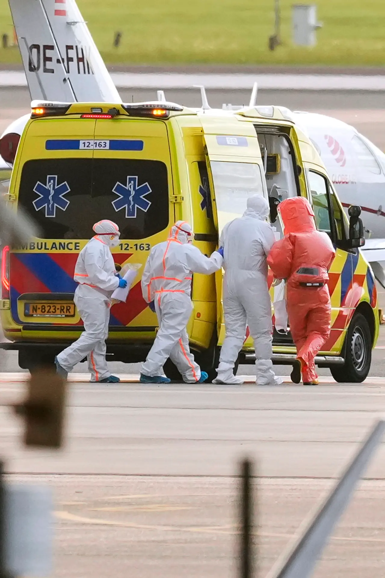 Zdravotný personál v špeciálnych ochranných odevoch pomáhajú pacientovi (druhý sprava) s podozrením na infekciu hantavírusom nasadnúť si do sanitky na letisku Schiphol v Amsterdame.