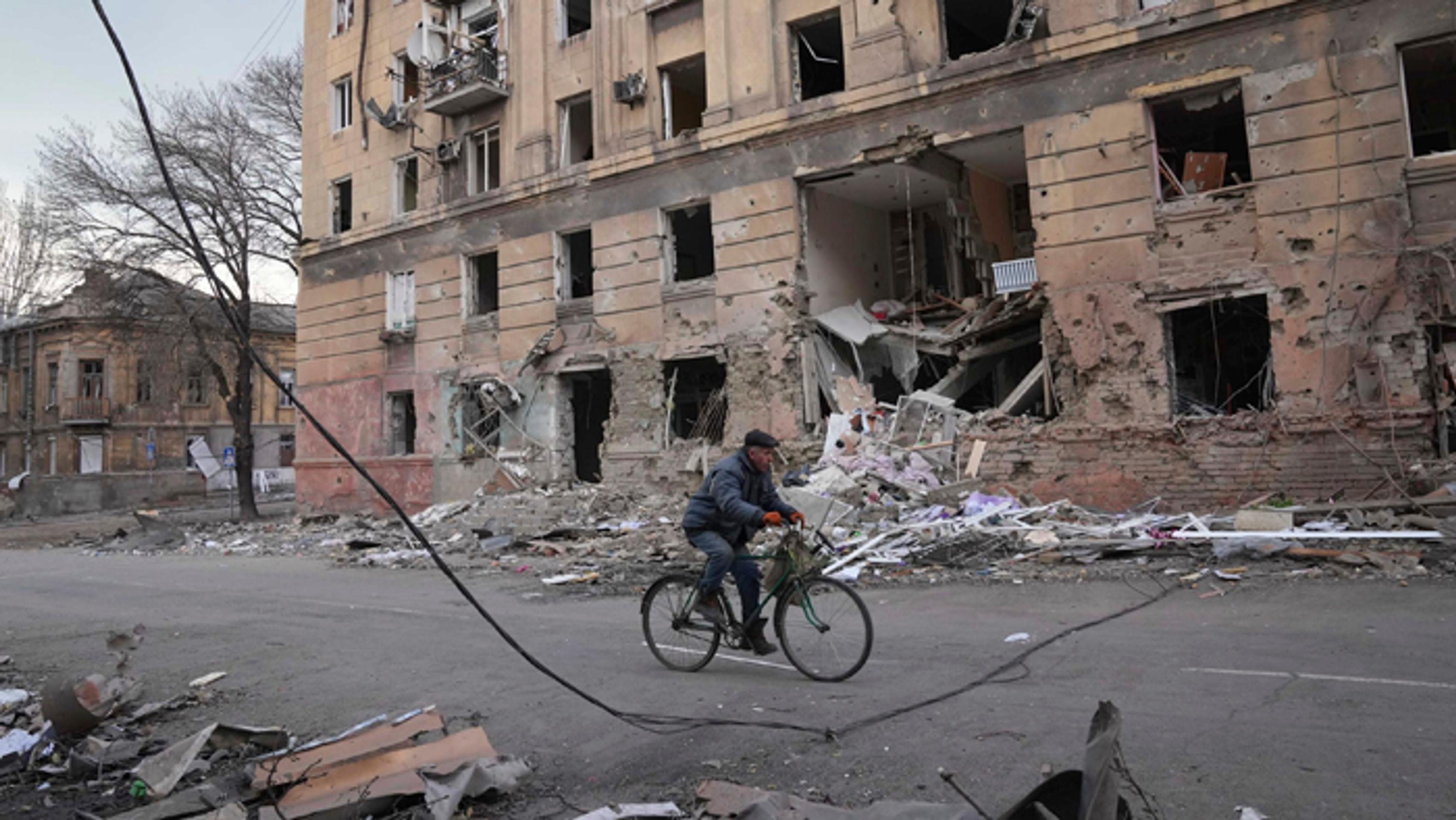 Muž jazdí na bicykli okolo budovy po ostreľovaní v Mariupole.