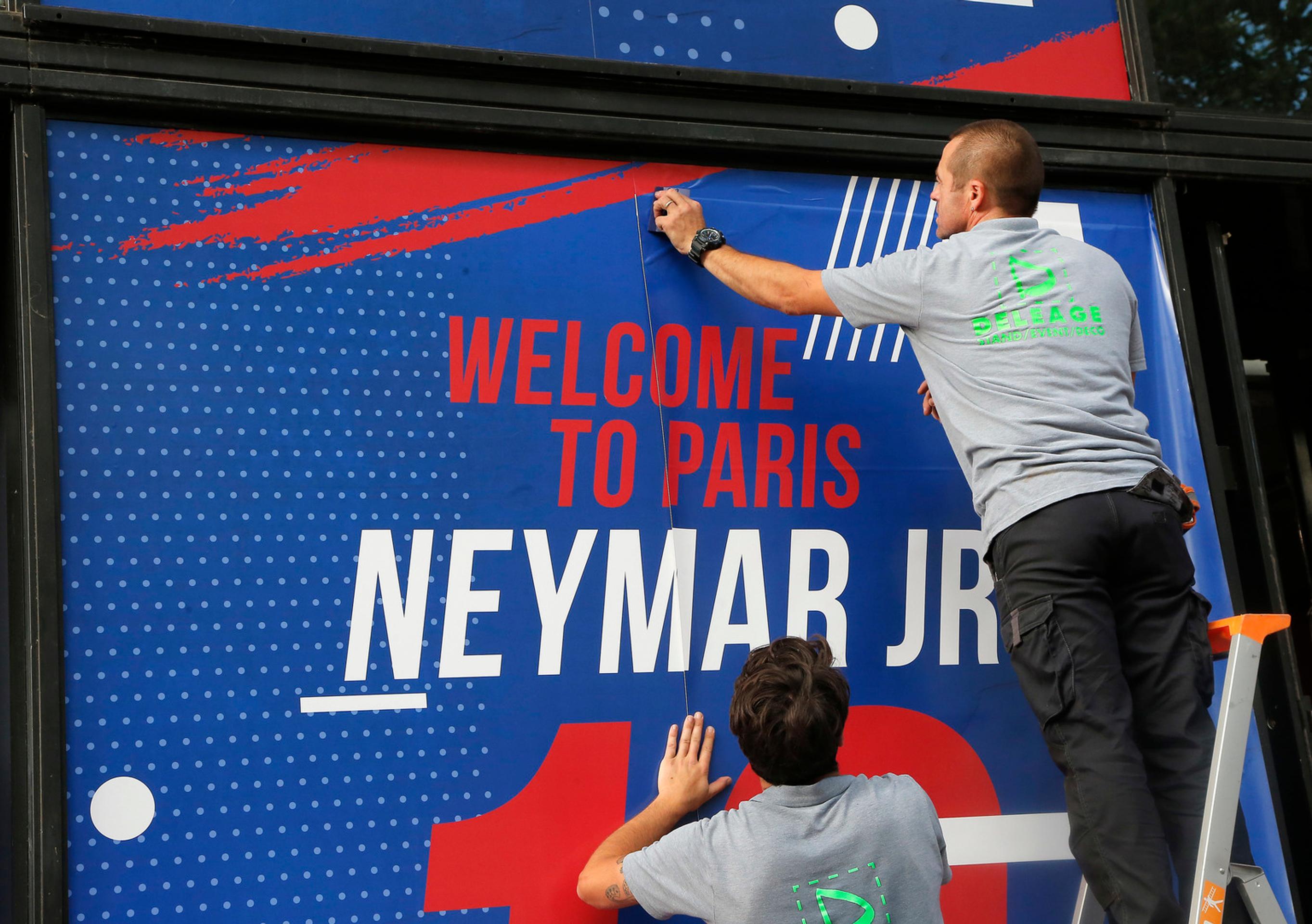 Zamestnanec pripevňuje uvítací transparent pre Brazílčana Neymara pred oficiálnym klubovým obchodom Paríža Saint-Germain.