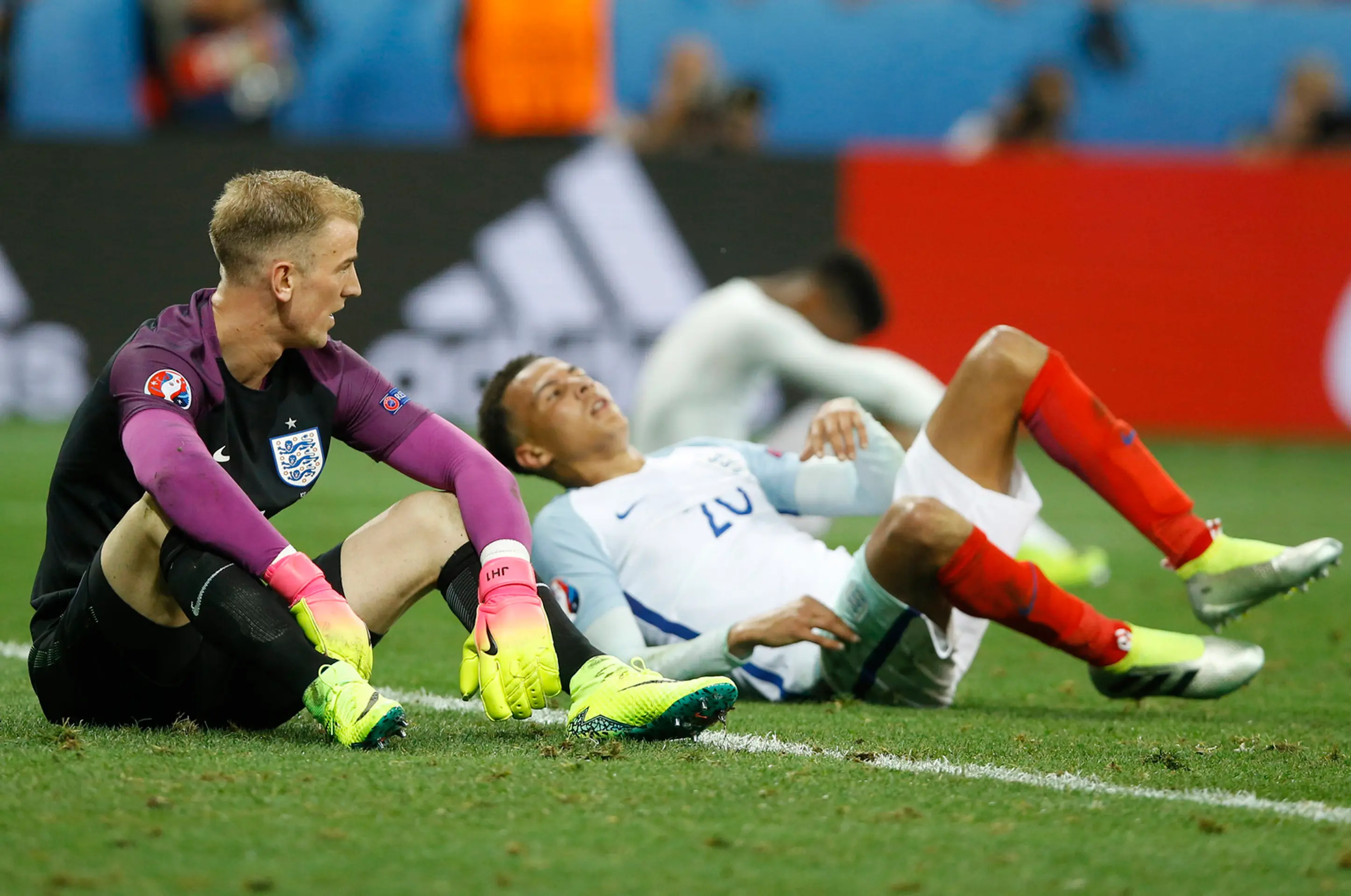 Anglickí futbalisti brankár Joe Hart (vľavo) a Dele Alli sedia na trávniku po osemfinálovom vypadnutí na ME s Islandom.