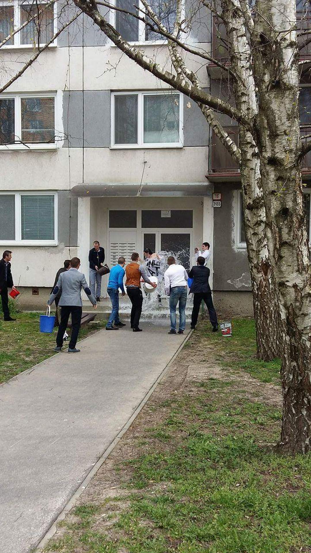 Mládenci v Leviciach oblievajú dievča pred panelákom.