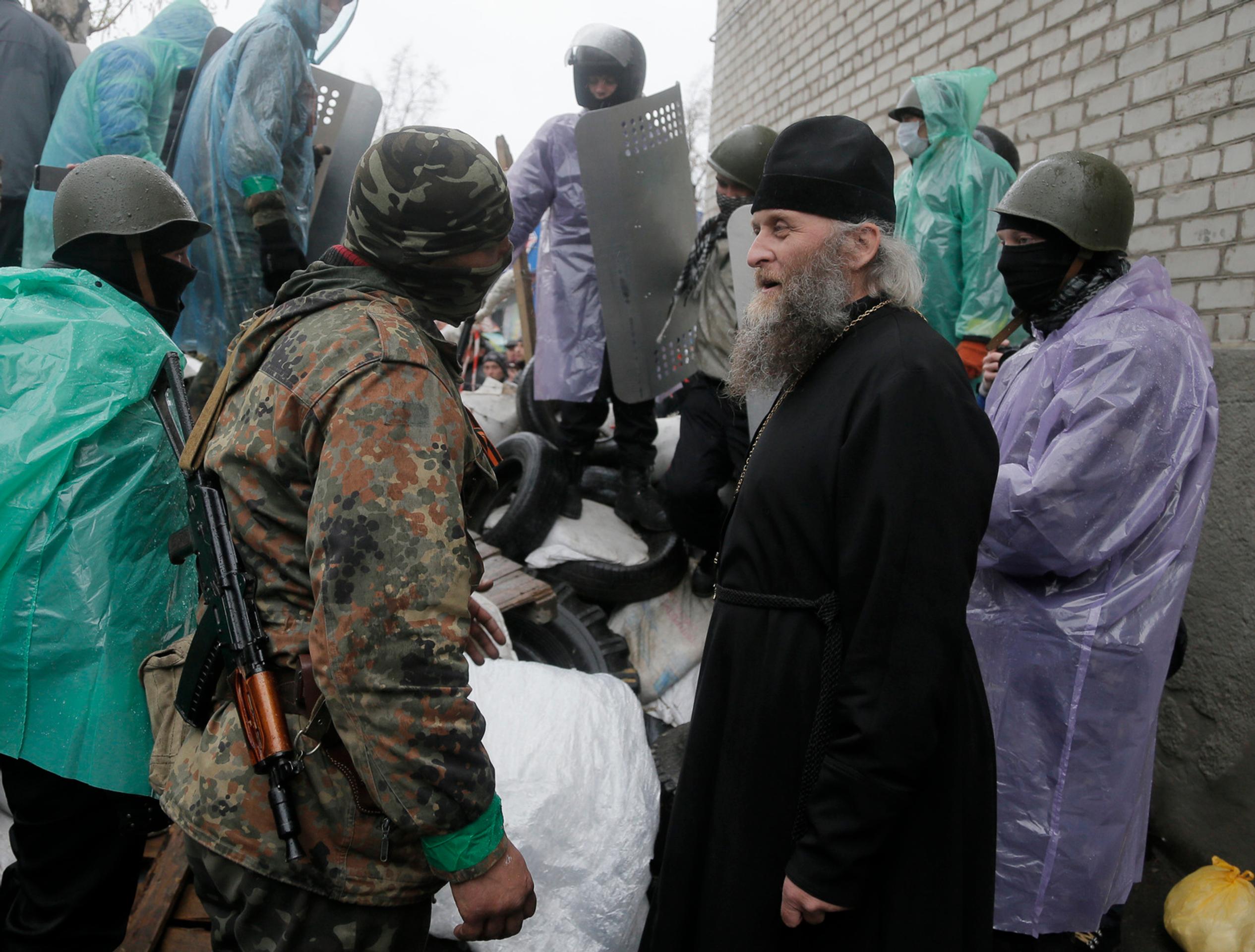 Pravoslávny kňaz sa rozpráva s proruským ozbrojeným strelcom pred obsadenou policajnou stanicou v ukrajinskom meste Slovjansk.