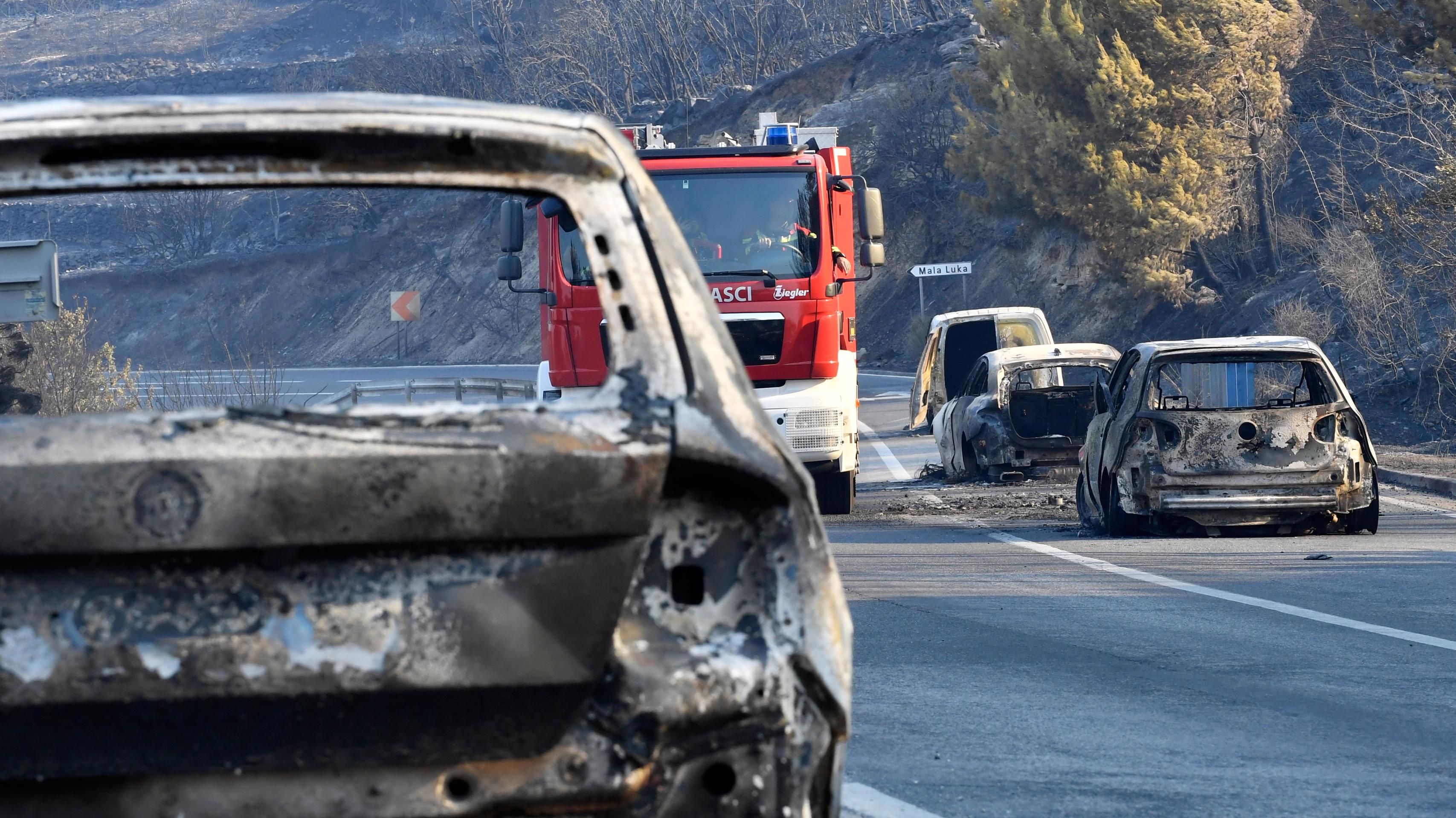 Po lesnom požiari na pobrežnej ceste pri Jadrane neďaleko Omiša sa medzi vyhorenými autami pohybuje hasičské vozidlo.