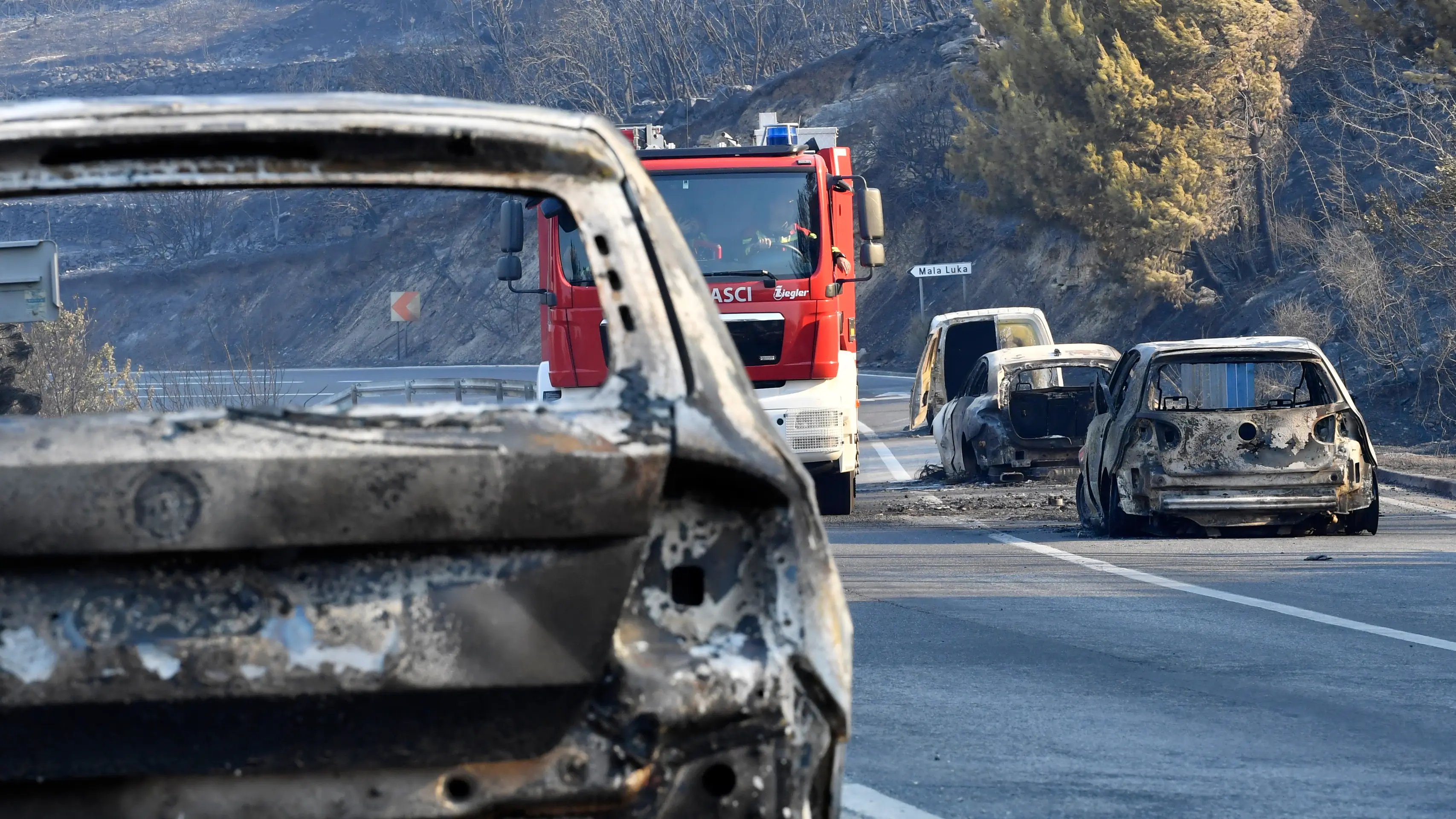 Po lesnom požiari na pobrežnej ceste pri Jadrane neďaleko Omiša sa medzi vyhorenými autami pohybuje hasičské vozidlo.