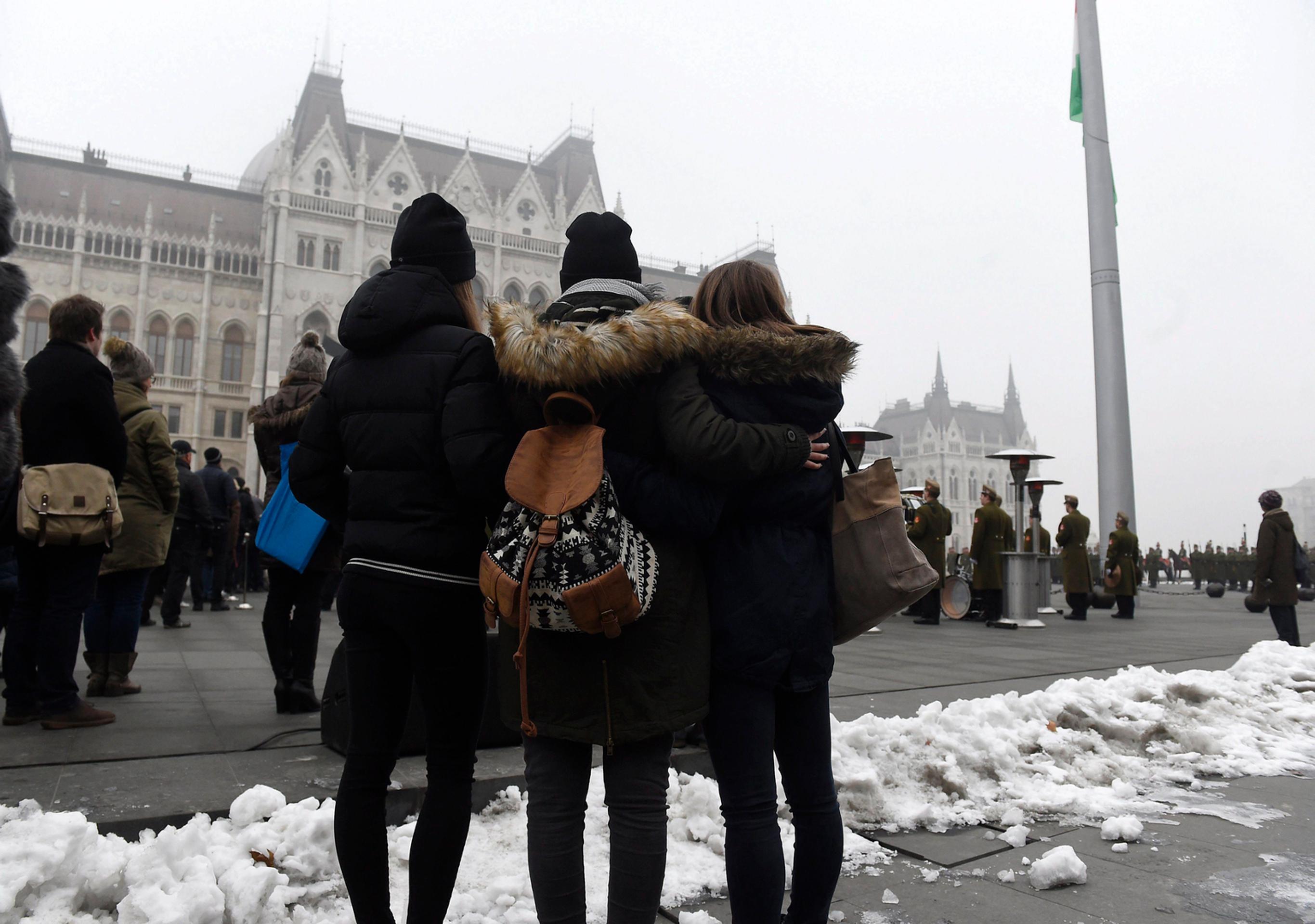 Ľudia sledujú spúšťanie štátnej vlajky na pol žrde.