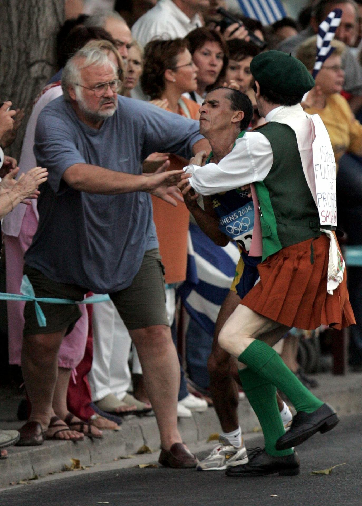 Neznámy muž v kostýme napadá favorita pretekov, brazílskeho atléta Vanderleia De Limu, na maratónskej trati v Aténach.